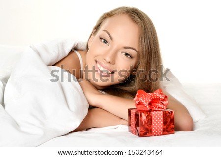 Portrait of a beautiful young woman with gift in white bed