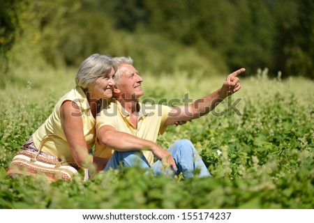 Beautiful happy old people sitting in the summer park. man pointing