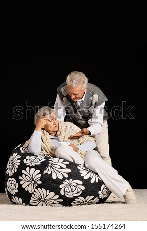 Old couple sitting on armchair on black background and drinking coffee