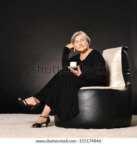Smiling senior woman portrait in black dress sitting on dark background