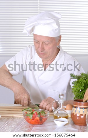 Elderly man chef cooking tasty vegetable salad