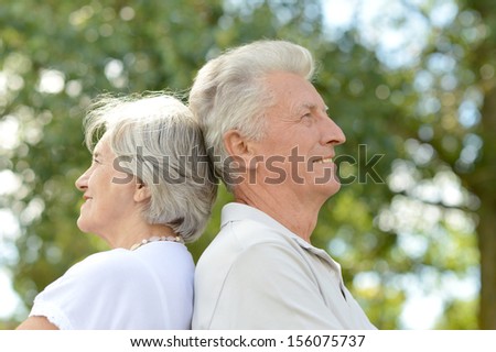 Happy senior couple standing back to back in summer park