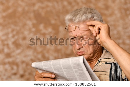 Elderly man reading newspaper on beige background