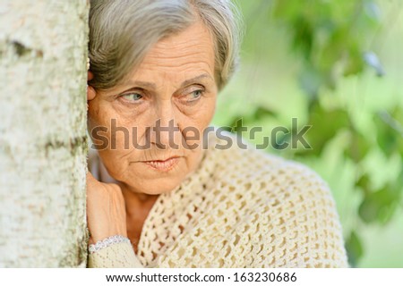 Portrait of sad elderly woma standing by a tree