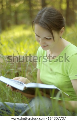 Nice woman reading a book at nature on a green summer meadow