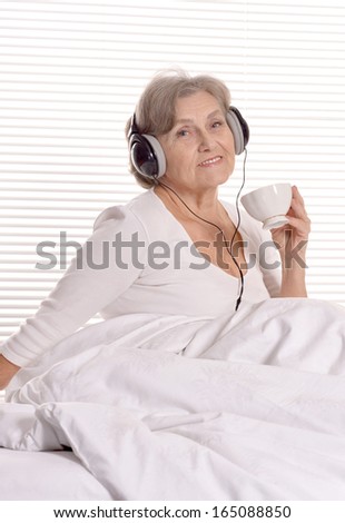 Happy senior woman listen a music in headphones resting in a bedroom