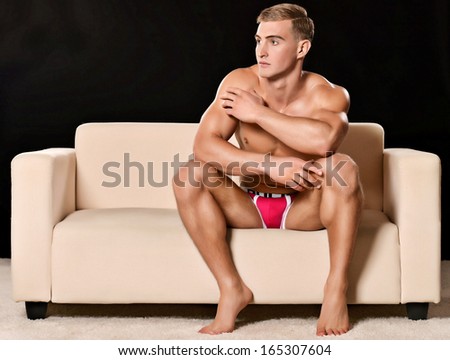 Sexy Man Sitting On Sofa Isolated On Dark Background