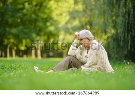 Sad elderly woman sitting on a grass in summer park