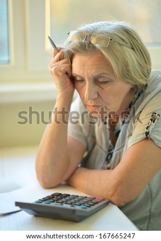 Serious elderly woman with calculator sitting at table