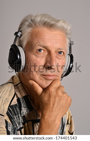Elderly man listen to music in headphones on grey background