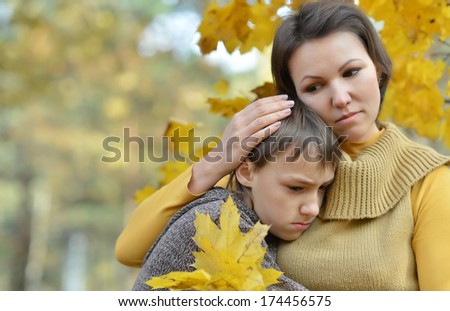 Beautiful sad mother with her son on a walk during the fall of the leaves in the park