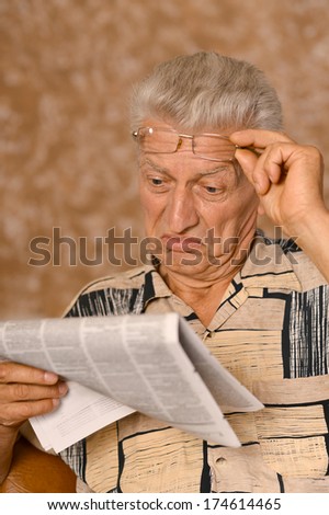 Elderly man reading newspaper on beige background