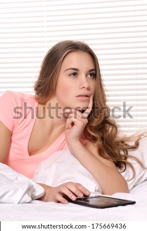 Young Caucasian woman lying in bed with tablet pc on a light background