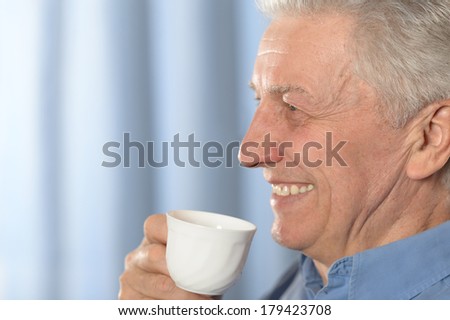 Happy old man drinking coffee on blue
