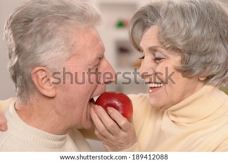 Close-up portrait of a happy senior couple eating apple at home
