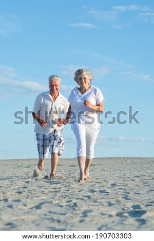 Old couple running on a beach in a sunny day