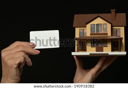 Older Woman holding miniature house and blank card on black background