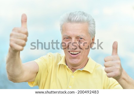 Old man showing thumbs up on blue sky background