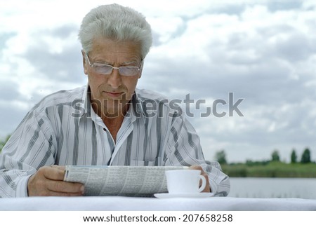 Attractive cute older man reading newspaper outdoors