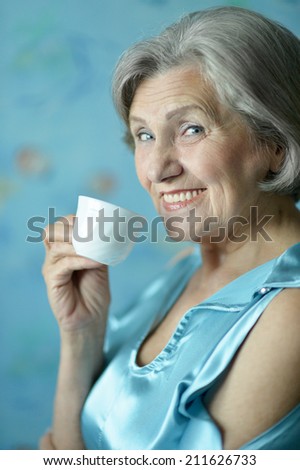 Portrait of happy retired woman drinking tea on blue background