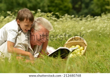 Happy grandfather and child reading book in summer forest