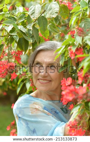 Close-up portrait of an older woman on walk with red flowers