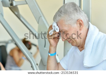 Elderly tired man in a gym with towel