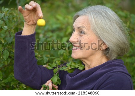 Elderly woman walking in the park, holding a fruit in her hand