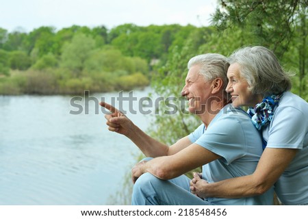 Happy senior couple sitting in summer near lake ,man pointing his finger
