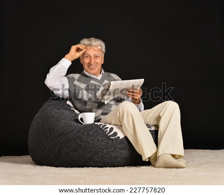 Elderly man reading newspaper sitting in armchair on white background