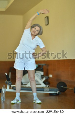 Smiling active mature woman stretching in gym