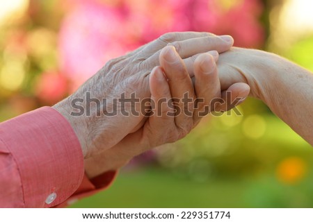 Elderly couple holding hands over natural background