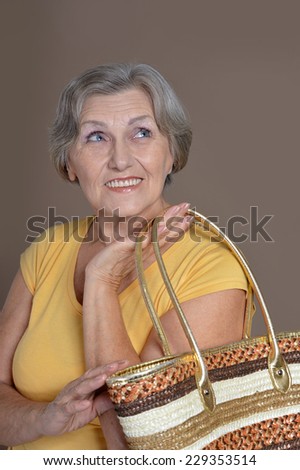 Portrait of happy elderly woman with bag on gray background