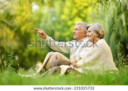 Beautiful happy old people sitting in the summer park. man pointing