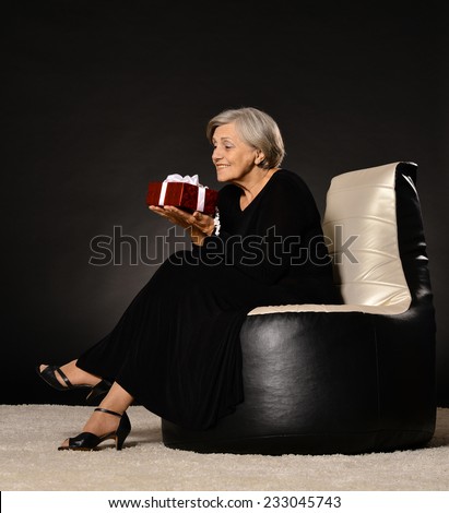 Happy elderly woman sitting with gift on black armchair
