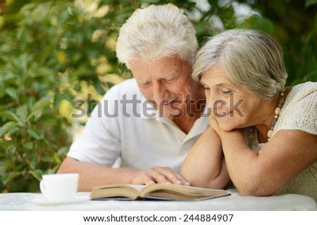 Beautiful older couple resting in the garden in summer ,reading a book