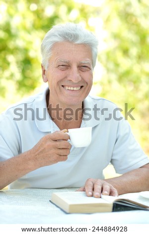 Handsome older man sitting at a table at home on the veranda with book