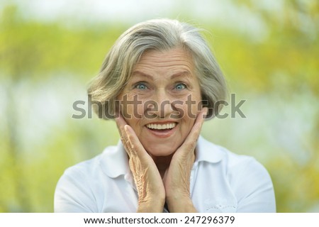 Senior happy woman smiling on background of green summer leaves
