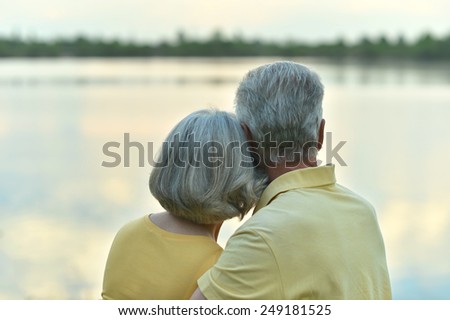 Happy senior couple in summer near lake during sunset,back view