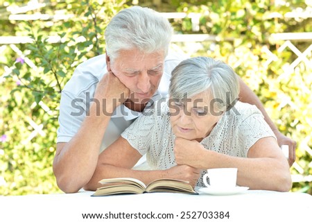 Beautiful older couple resting in the garden in summer ,reading a book