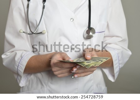 Female doctor with money, standing on grey background