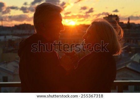 Silhouettes of elderly couple in love over sunset sky