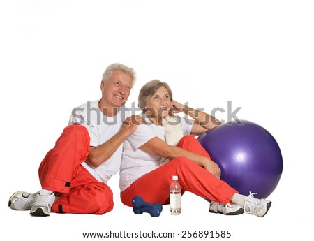 Elderly couple exercising,sitting on a floor of a gym isolated on white