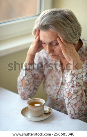 Portrait of a sad old woman drinking tea
