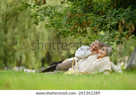 Happy elder couple resting on grass in park with apples