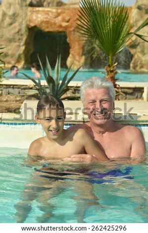 Grandfather swimming with grandson in blue pool water