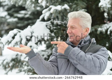 Senior man standing outdoor in winter pointing by his hand