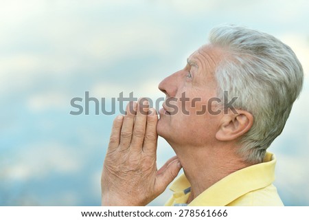 Thoughtful senior man prays in nature close-up