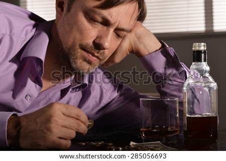 Young man sleeping with whiskey and money at table