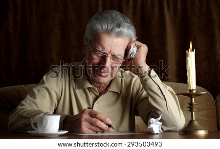 Elderly pensive man writes a letter by candlelight